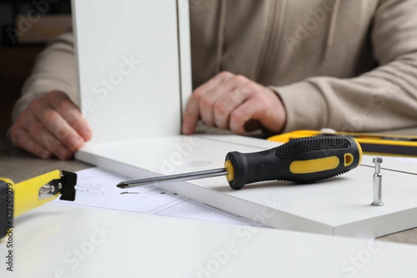 Fototapeta Man assembling wooden furniture at table, focus on screwdriver