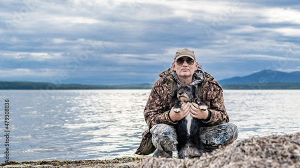 Fototapeta Happy pensioner sits with dogs on the seashore. Satisfied with rest.