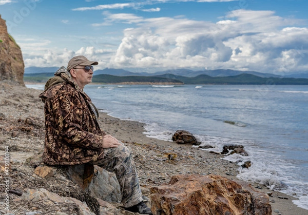 Fototapeta Portrait of a pensive elderly man on the seashore looking at the sea against the backdrop of rocks thinking about the meaning of life.imagination and vision of a happy future.