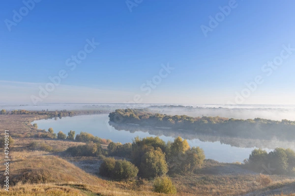 Fototapeta Autumn landscape in the early morning overlooking the river. A wide river and endless expanses of fields. Yellow leaves on trees and bushes are illuminated by the rays of the rising sun.