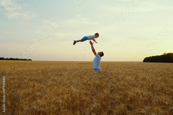 Fototapeta Father throwing little son up in the air in wheat field in slow motion. Parent and child having fun and enjoying time together. Concept of happiness