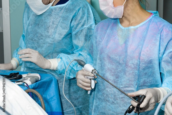 Fototapeta The surgeon holds a surgical laparoscopic manipulator in his hands. Selective focus. Minimally invasive laparoscopic proctological surgery. A doctor in uniform and gloves uses a surgical instrument.