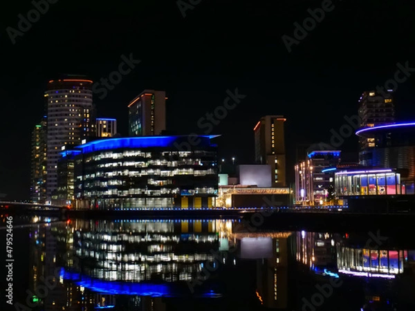 Obraz Vibrant reflections of modern buildings in Salford, Greater Manchester on calm dark water at night, copy space.