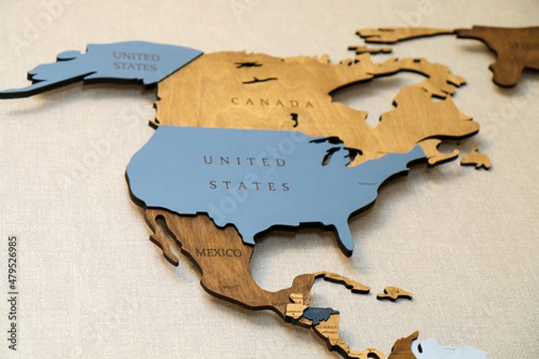 Fototapeta Wooden map of the world on the wall.  Mainland North America continent with the names of countries and capitals. Geographic concept of plywood, laser cutting.
