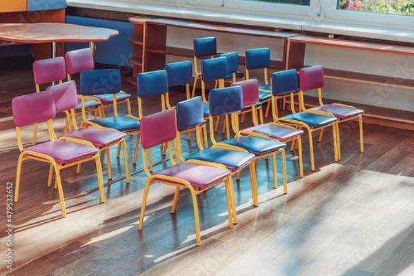 Fototapeta Empty preschool classroom with multi colored chairs standing in rows