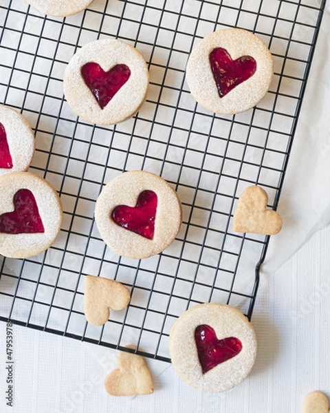 Fototapeta Close up image of heart shaped Linzer cookies arranged on a cooling rack. Red hearts biscuits fill the frame in flat lay top down view. Love, romance and valentines day food concept with copy space