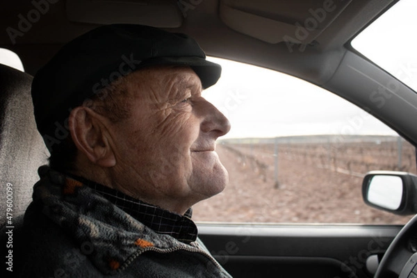 Obraz Old man smiling is driving by the countryside wearing a cap