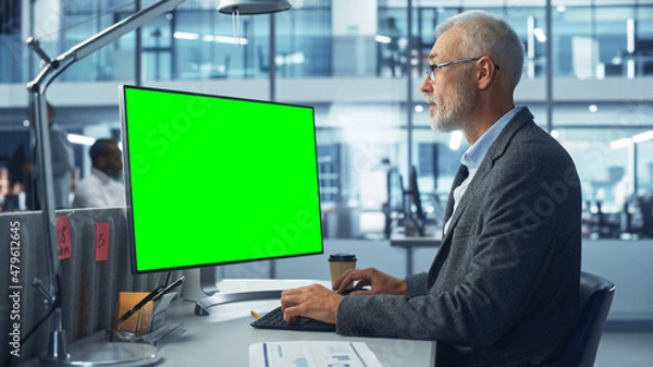 Fototapeta Diverse Modern Office: Senior Caucasian IT Technician Using Desktop Computer with Green Chroma Key Screen. Engineer Administrator Work on e-Commerce Development, Project Marketing, Big Data Analysis