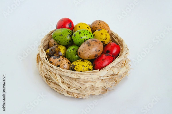 Fototapeta Quail eggs painted in different colors in a light wicker basket on a white background
