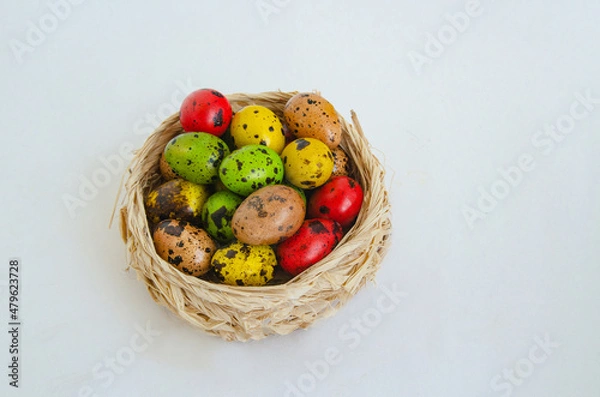 Fototapeta Quail eggs painted in different colors in a light wicker basket on a white background