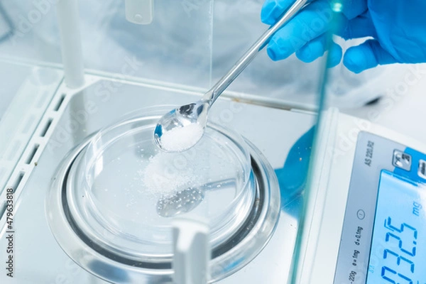 Obraz Close up scientist hands in rubber gloves use metal spatula for weighing white powder of the substance using digital balances. Preparation to clinical or pharmaceutical analysis