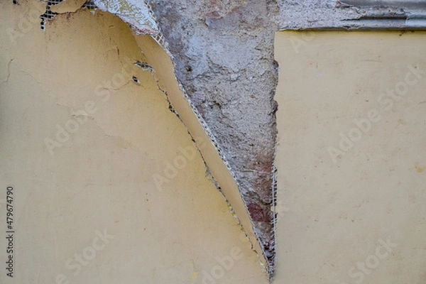 Fototapeta Exterior wall of a building with damaged stucco. Demonstration of poor-quality insulation of buildings. Thin layer of plaster and reinforcing mesh. Construction and repair. Selective focus. Close-up.