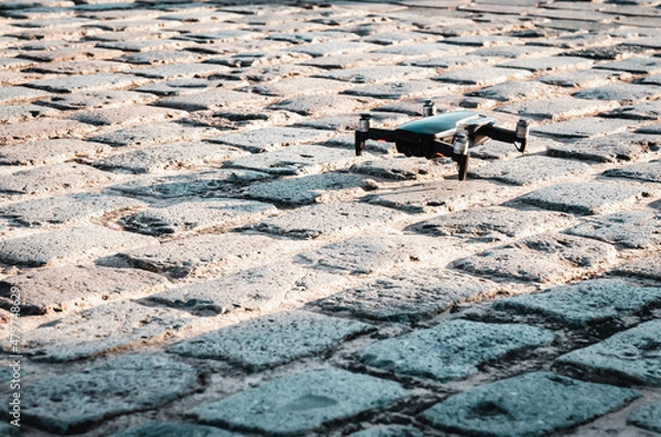 Obraz A quadrocopter drone hovering over cobblestone pavement,