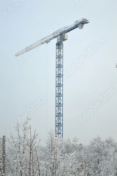 Fototapeta working tower crane at a construction site, snowy winter