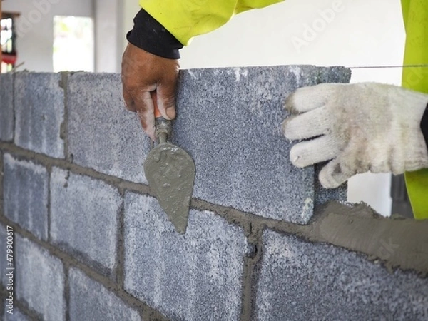 Obraz Bricklayer is laying bricks on the outer wall with a trowel. closeup photo, blurred.