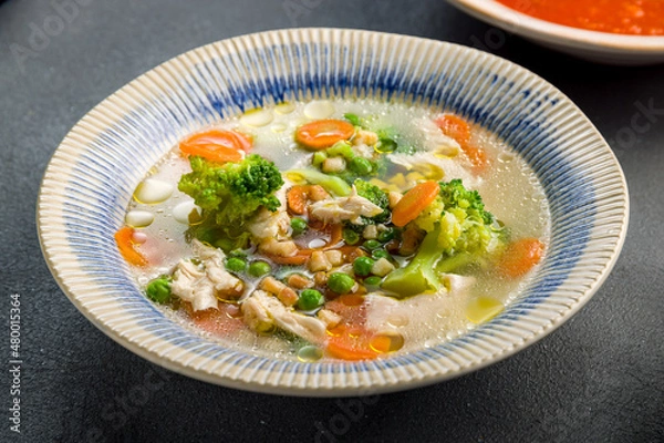 Fototapeta Chicken soup bouillon in a plate with vegetables on grey concrete table macro close up