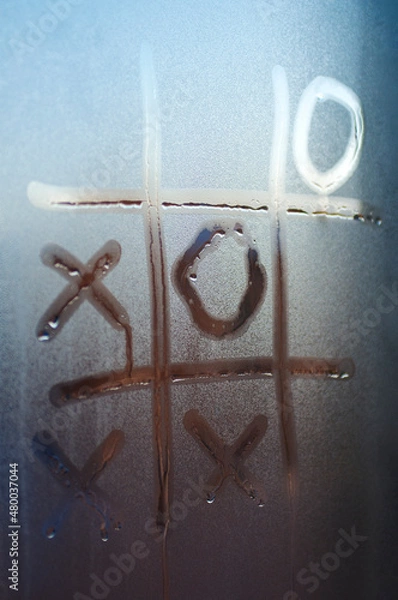 Fototapeta The concept of loneliness during the coronavirus pandemic. Tic-tac-toe is painted on the misted glass.