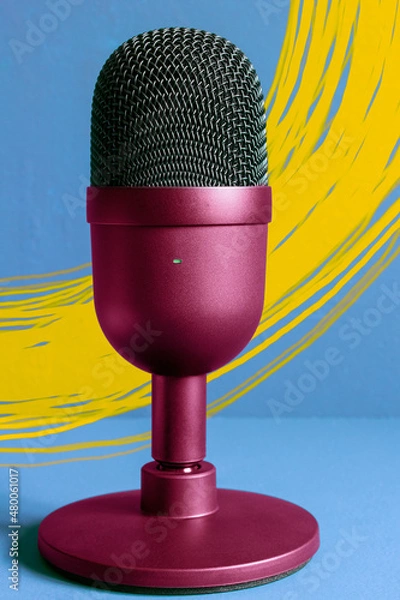 Fototapeta A modern presentation of a colorful design microphone against a sky blue wall painted with yellow brushstrokes highlights the product with the green light on. Communication and business.