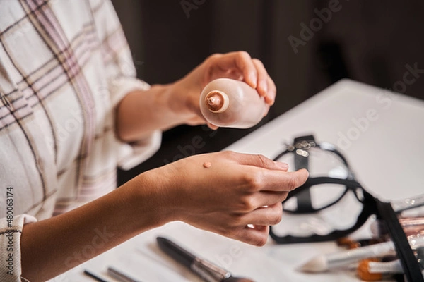 Fototapeta Blogger woman putting drop of her tone cream at hand while broadcasting make up tutorial