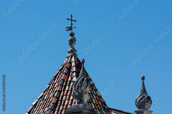 Fototapeta Old colored roof tiles with a vane, a cross and ornaments in Coimbra, Portugal.