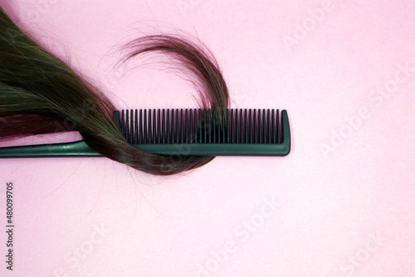 Fototapeta A lock of female light brown hair, a comb on a pink background.