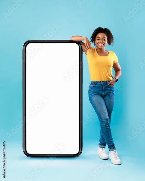 Obraz Mobile app ad. Black woman leaning on huge smartphone with empty screen, advertising new website or application, mockup