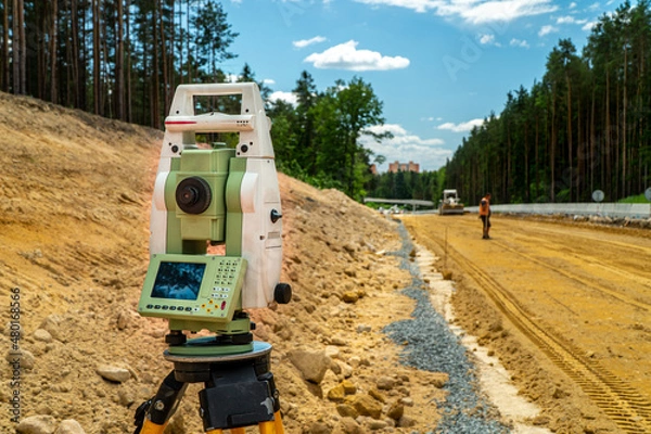 Fototapeta Surveyors equipment (theodolite or total positioning station) on the construction site of the road or building with construction machinery background