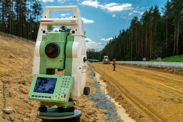 Fototapeta Surveyors equipment (theodolite or total positioning station) on the construction site of the road or building with construction machinery background