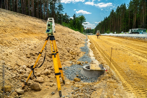 Fototapeta Surveyors equipment (theodolite or total positioning station) on the construction site of the road or building with construction machinery background
