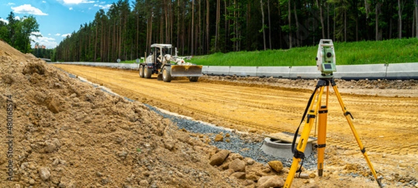 Fototapeta Surveyors equipment (theodolite or total positioning station) on the construction site of the road or building with construction machinery background