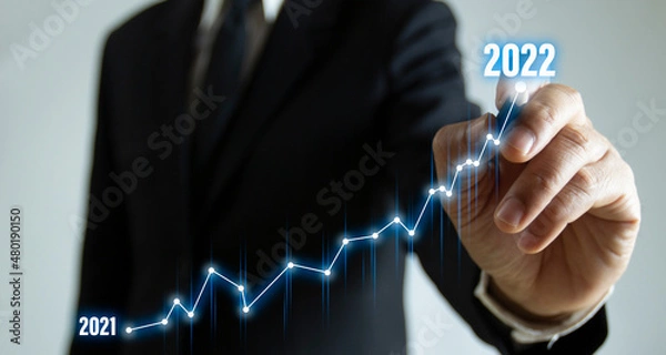 Fototapeta Business plan for increase in 2022 year.Business person draws increase arrow graph corporate future growth year 2021 to 2022. Development to success and motivation.New year with great achievements