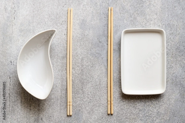 Fototapeta White empty plates and bamboo chopsticks on gray background with copy space