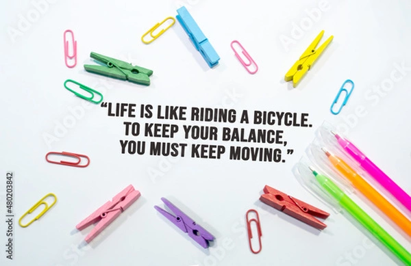 Fototapeta Life is like riding a bicycle. To keep your balance, you must keep moving, motivational quote stationery items on white background 