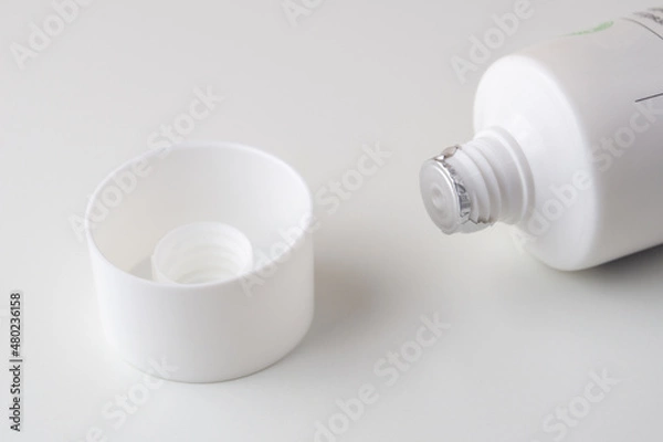 Fototapeta Sealed white tube of ointment and cap on a white background. A tube of cream covered with protective foil. The cap removed from the tube of cream.