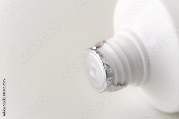 Fototapeta The tube of cream is sealed with protective foil. White tuba on a white background. Screw thread close-up. Copy space.