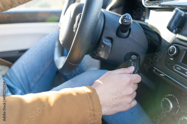 Fototapeta Young eastern man casually dressed with hands holding driving wheel, starting engine turning on ignition key in car on sunny day. No face, anonymous, travel, exam, lesson, learning, taxi driver