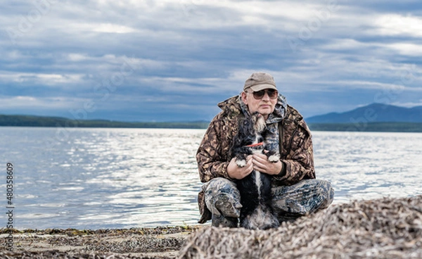 Fototapeta Happy pensioner sits with dogs on the seashore. Satisfied with rest.