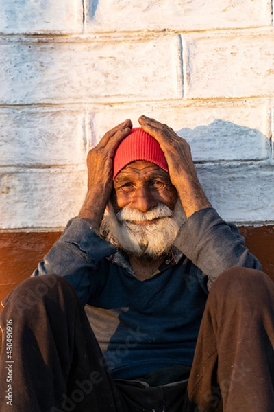 Fototapeta portrait of an old indian man, old aged man with wrinkles on his face holding his face with his hands and sitting in the sunlight.