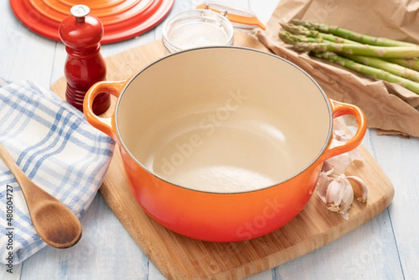 Obraz Orange dutch oven on wooden board with ingredients around it