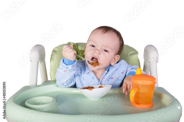 Obraz child is eating sitting at table, isolated over white