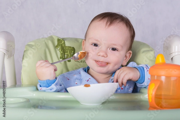 Obraz child is eating sitting at table, isolated over white