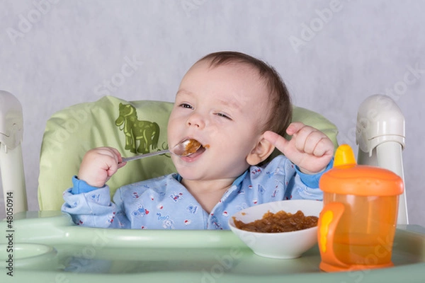 Obraz child is eating sitting at table, isolated over white