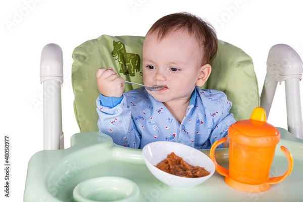 Obraz child is eating sitting at table, isolated over white