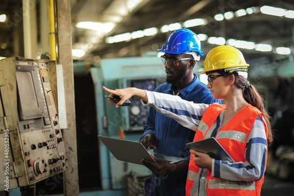 Obraz Caucasian woman programmer engineer and Indian man Technician operator machine is working in factory, checking lathe machinery operating with laptop to maintain safety of work, Safety first concept.