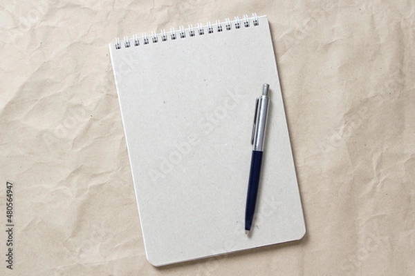 Obraz Gray notepad with white coiled spring and pen on a background of beige crumpled craft paper. With empty space for text and design