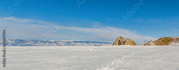 Fototapeta View of the frozen Lake Baikal and the mountains on a winter sunny day. Sacred Shamanka Mountain on Olkhon Island. Tourists walk on the ice, admire the beauty of the ice. Panorama.