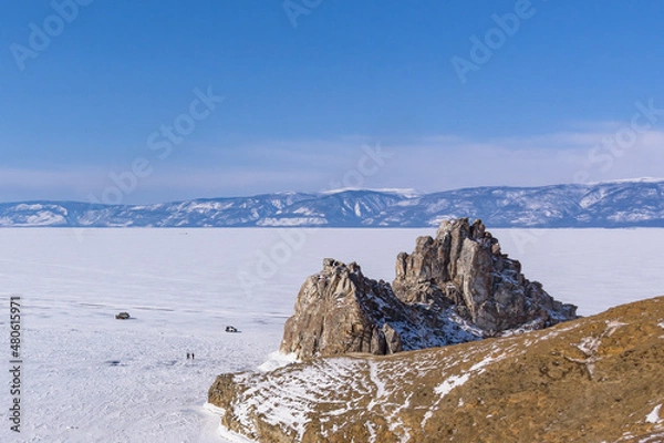 Fototapeta Sacred Shamanka Mountain on Olkhon Island in winter. View of the frozen Lake Baikal on a sunny day. View from above. Below, tourists walk on the ice