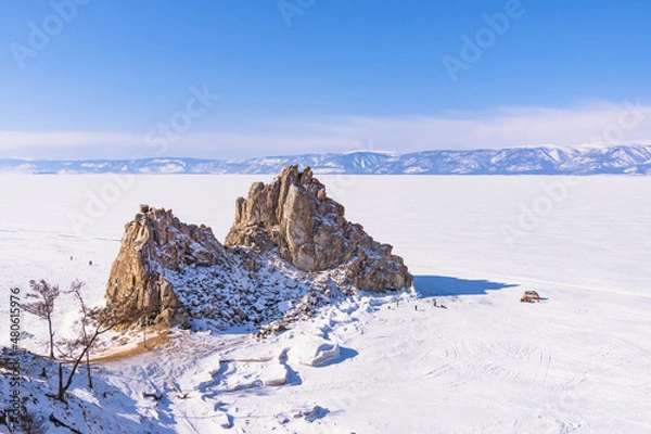 Fototapeta Sacred Shamanka Mountain on Olkhon Island in winter. View of the frozen Lake Baikal on a sunny day. View from above. Below, tourists walk on the ice
