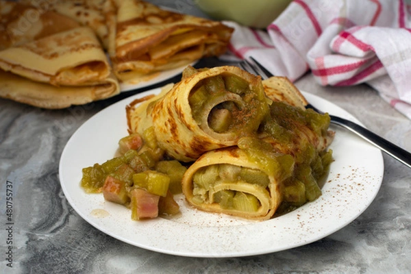Fototapeta Thin German Pancakes (like French crepes) with sweet caramelized rhubarb filling, served with loads of cinnamon and sugar. The pancake is the classic from the kitchen of our childhood.