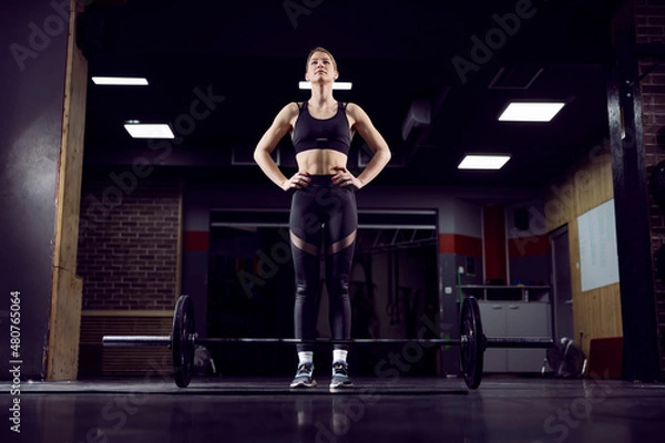Fototapeta A strong young woman standing in the gym and preparing to lift weights.